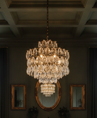 A large multi-tiered crystal chandelier with a gold-toned frame hangs in a grand room with dark gray walls, a coffered ceiling, and two mirrors.