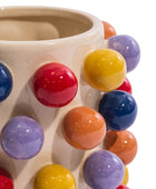 Close-up of a ceramic mug with a cream-colored glaze and raised, glossy multicolor spherical accents in red, yellow, blue, purple, and orange on a white background.