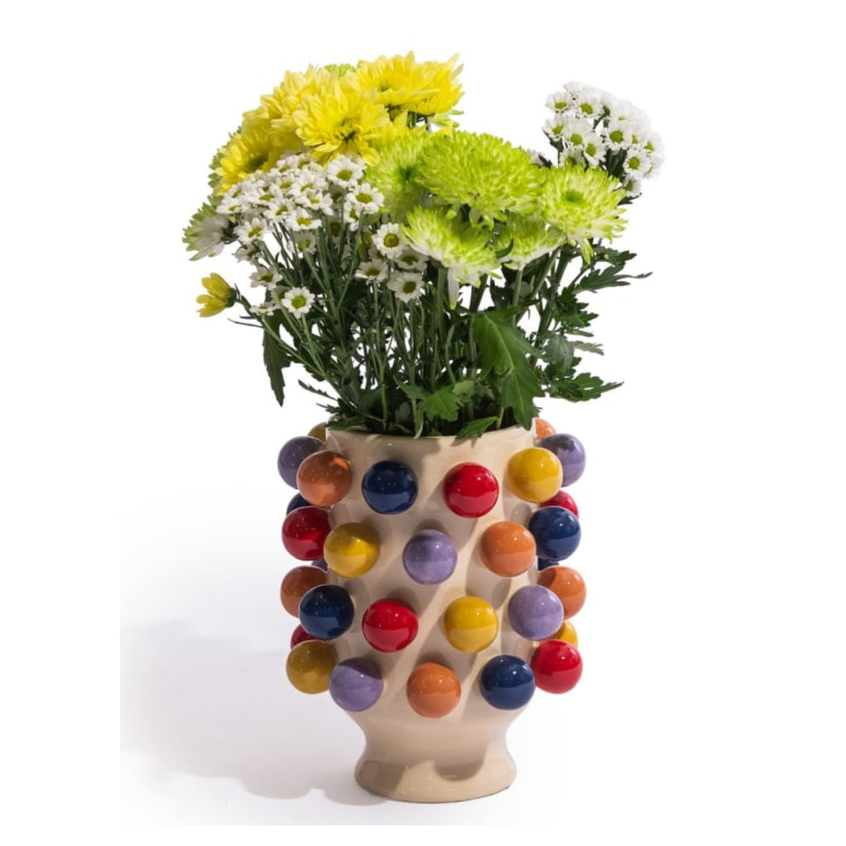 A beige ceramic vase covered in colorful glossy spherical bumps, filled with yellow, green, and white daisies, photographed on a white background.
