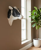 Decorative cow head on a wall next to a window with a plant in the corner.