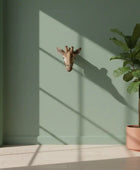 Giraffe head sculpture on a green wall with a potted plant below