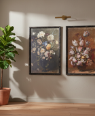 Two floral paintings on a wall with a plant and side table in the foreground.