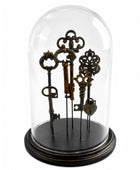 A set of five antique-style decorative keys displayed inside a clear glass dome cloche on a round black base, photographed against a plain white background.