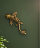 Gold fish-shaped wall decor on a green wall with a plant and window in the background