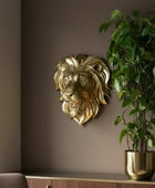 Gold lion head wall decoration next to a potted plant on a shelf against a brown wall.