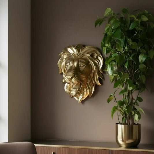 Gold lion head wall decoration next to a potted plant on a shelf against a brown wall.