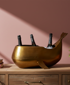 Brass wine cooler with bottles on a wooden surface against a pink wall