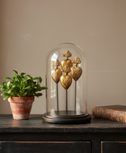 Decorative gold sculpture under a glass dome on a wooden surface with a plant and book in the background.