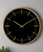 Black wall clock with gold accents on a gray background