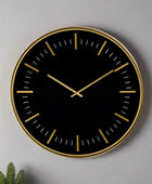 Black wall clock with gold accents on a gray background