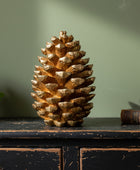 Decorative gold pine cone on a dark wooden surface with a green plant and book in the background.