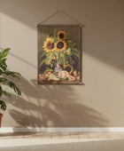 Tapestry of sunflowers hanging on a beige wall with a potted plant below.