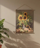 Framed artwork of sunflowers and fruits on a beige wall with a plant beside it.