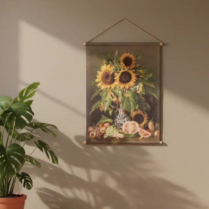 Framed artwork of sunflowers and fruits on a beige wall with a plant beside it.