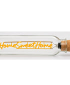 A clear glass bottle with a cork stopper, featuring a warm yellow-orange LED light string that spells out 'Home Sweet Home' in script and block lettering.