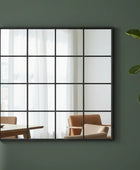 Decorative mirror with a black frame on a green wall, reflecting a room with furniture.