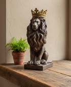 A bronze lion statue wearing a gold crown, displayed on a rustic wooden windowsill next to a small potted green plant against a textured beige wall.