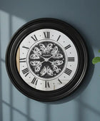 Decorative wall clock with black frame and white face on a blue wall with a plant to the right.