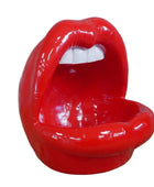 Red lips-shaped chair on a wooden surface with a stone wall background