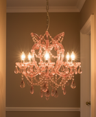 A pink crystal chandelier with six lit candle-style bulbs hanging in a hallway with warm beige walls.