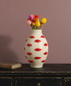 Vase with red lip designs and colorful tulips on a wooden surface against a purple wall