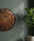 Large round copper clock on a wall with a potted plant beside it.
