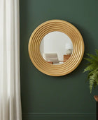 Round wooden mirror on a green wall with a plant and window in the background