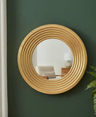 Round wooden mirror on a green wall with a chair and lamp in the reflection