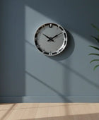 Wall clock on a gray wall with a plant on a wooden floor