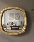 Gold-framed mirror on a wall reflecting a living room with a sofa and coffee table.