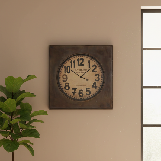 Decorative wall clock on a beige wall with a plant to the left.