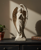Statue of an angel on a wooden surface with a plant and book in the background