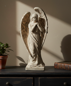 Statue of an angel on a table with a plant and book in the background