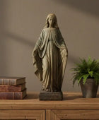Statue of a draped figure on a wooden surface with books and a plant
