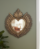 Decorative heart-shaped mirror with leaf-like designs on a green wall.