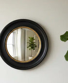 Round black-framed mirror on a wall with decorative items around it.
