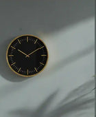 Black wall clock with gold trim on a light gray wall