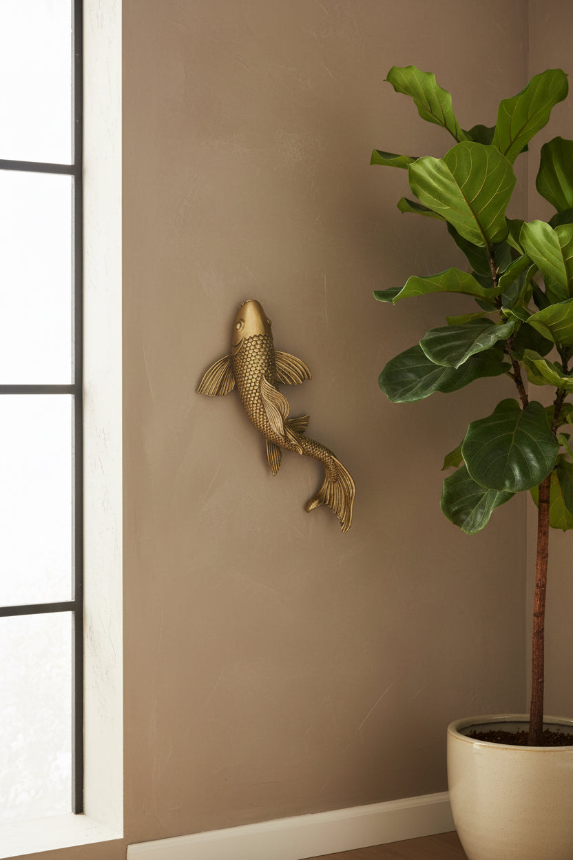 Gold fish wall sculpture on a beige wall next to a potted plant
