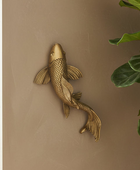 Gold fish wall decoration on a beige wall with a plant in the corner