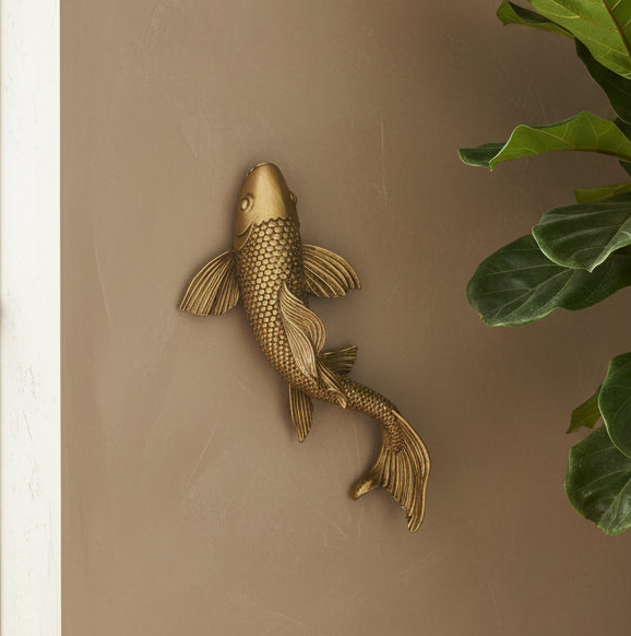 Gold fish wall decoration on a beige wall with a plant in the corner