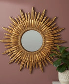 Decorative gold sunburst mirror on a brown wall with a plant in the corner.