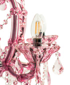 Close-up of a pink crystal chandelier detail with a clear flame-tip bulb, faceted pink glass arms, hanging crystal drops, and a visible filament light bulb on a white background.