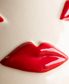 A glossy red lip-shaped decorative object or accessory on a plain off-white background, with partial matching red shapes visible at the top corners.