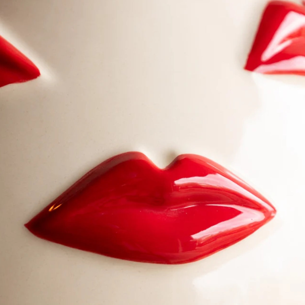 A glossy red lip-shaped decorative object or accessory on a plain off-white background, with partial matching red shapes visible at the top corners.