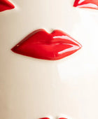 A close-up of glossy red lips molded onto a smooth off-white surface, with partial matching red lip shapes visible around the edges.