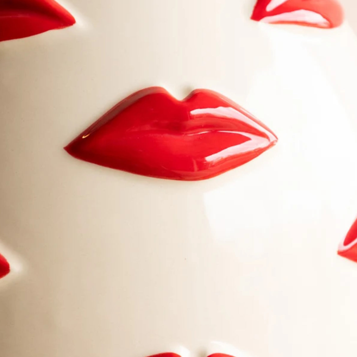 A close-up of glossy red lips molded onto a smooth off-white surface, with partial matching red lip shapes visible around the edges.