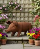Terracotta pig statue surrounded by potted flowers in a garden setting.