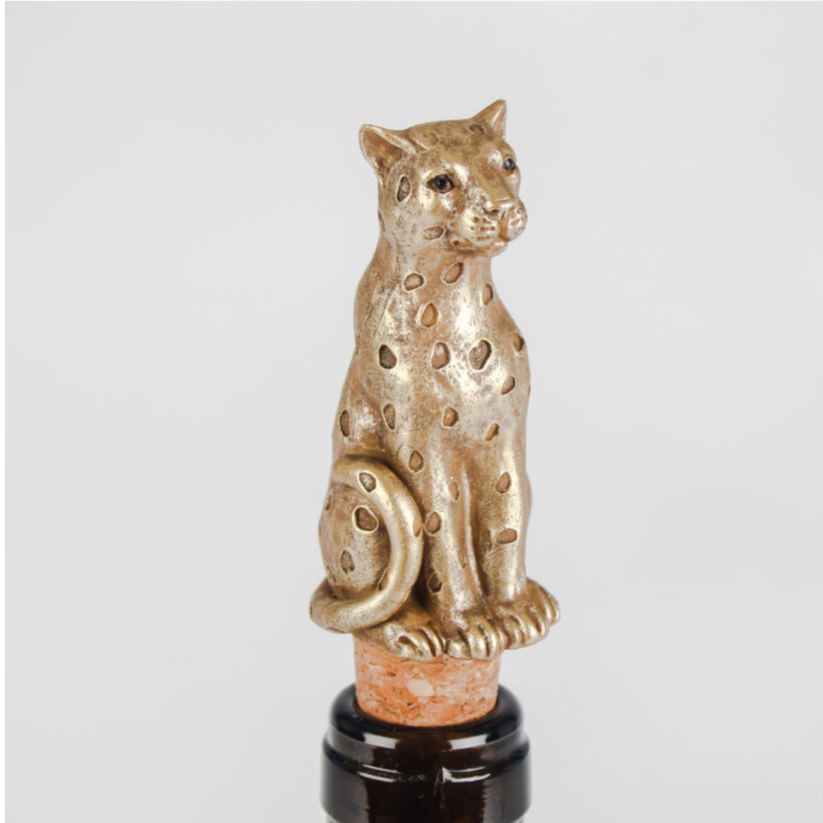 A metallic gold leopard-shaped bottle stopper with spotted detailing, mounted on a cork and dark glass bottle against a light gray background.