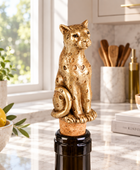 A decorative gold-toned leopard figurine corkscrew stopper sits on a cork inserted into a dark wine bottle on a marble kitchen countertop, with lemons, plants, and kitchen items in the background.