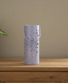 Purple decorative vase with butterfly design on a wooden surface next to a plant